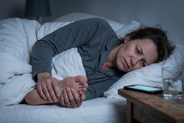Femme tenant son talon douloureux la nuit dans son lit, illustration de la douleur au talon nocturne
