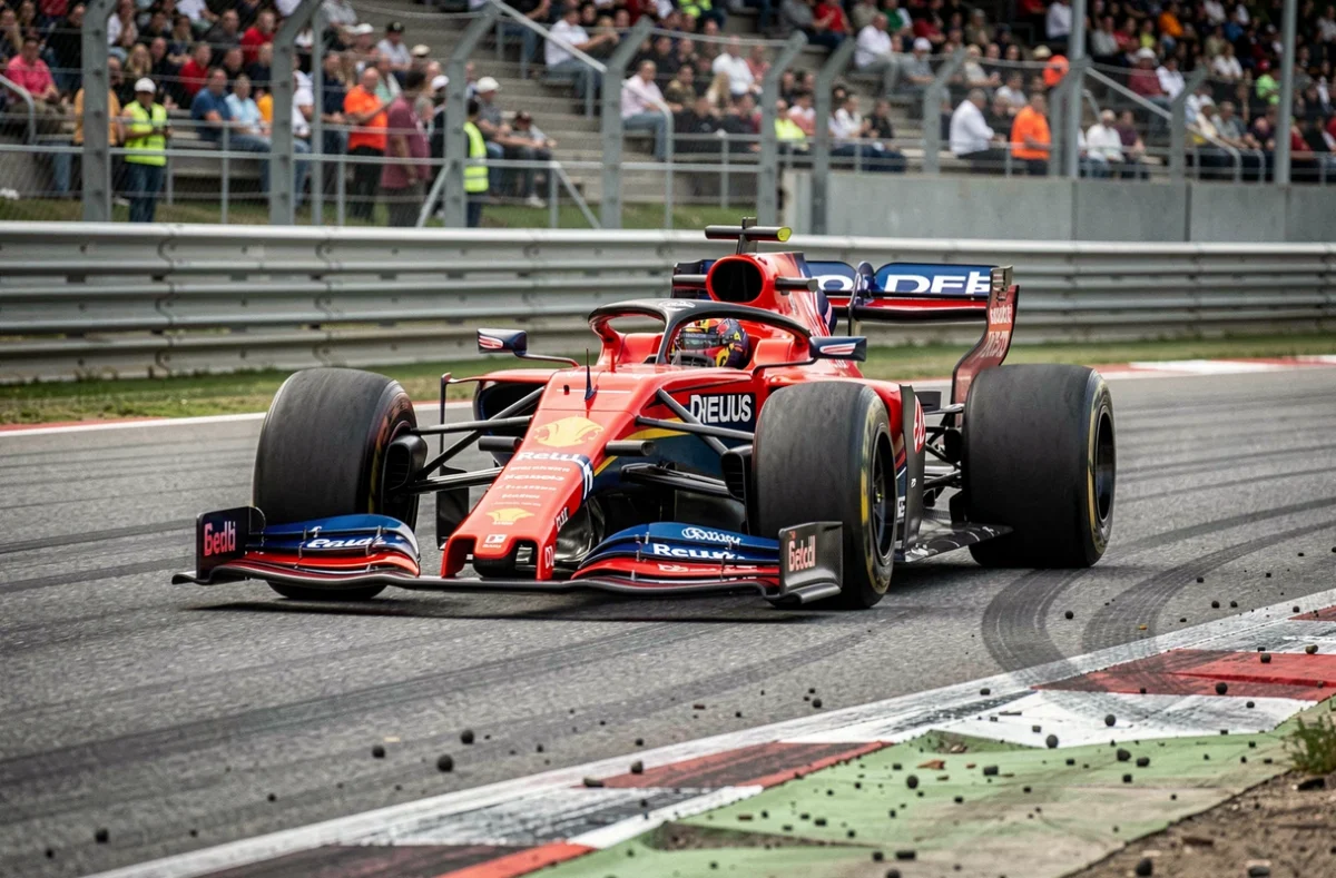 Monoplace de Formule 1 en plein virage sur un circuit moderne, avec les tribunes en arrière-plan floutées et la texture de l'asphalte visible au premier plan