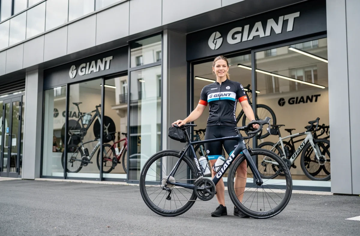 Cycliste en tenue Giant devant la devanture moderne du magasin Giant Toulouse Montaudran, avec des vélos haut de gamme visibles en vitrine