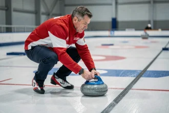 Joueur de curling en position de livraison relâchant une pierre de granit sur la glace lors d'une manche officielle